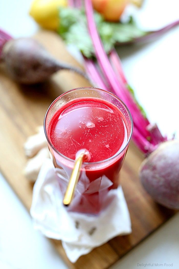 a glass filled with red liquid sitting on top of a cutting board next to vegetables