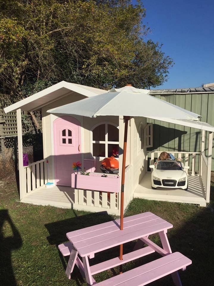 a small pink and white house with an umbrella over it's porch, next to a picnic table