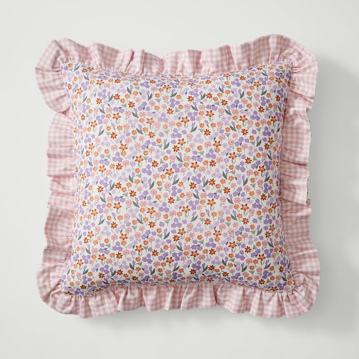 a pink and white flowered pillow with ruffles on the bottom, against a white background