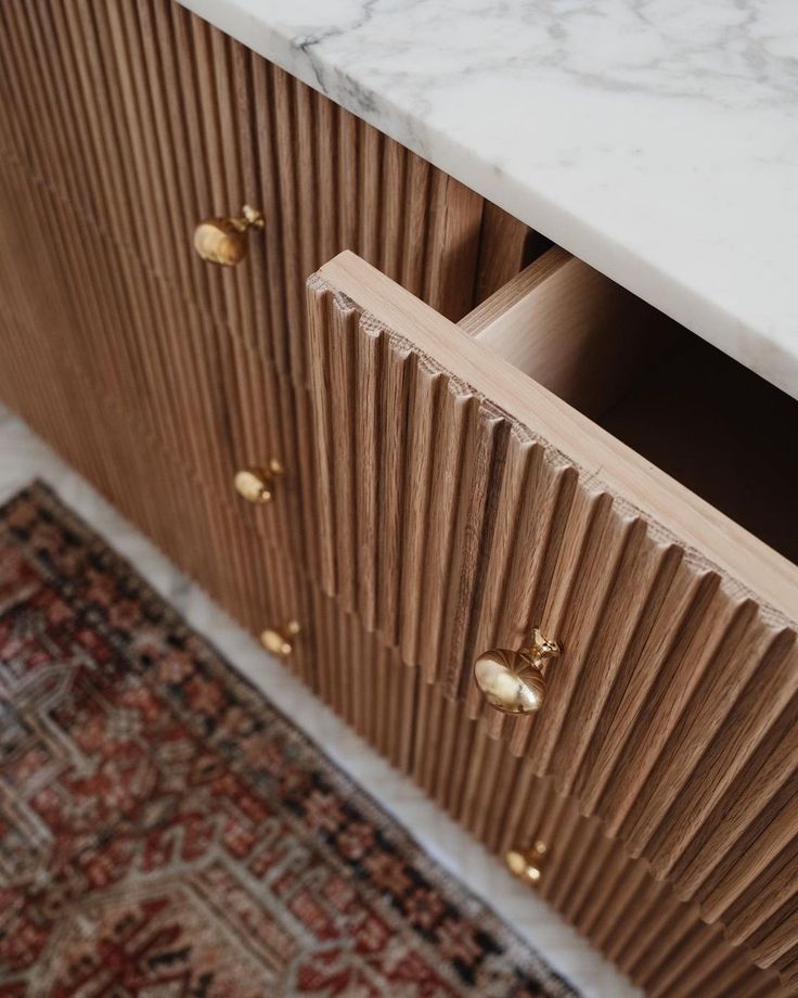 a white marble counter top sitting next to a wooden cabinet with brass knobs on it