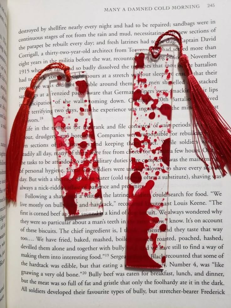 two bookmarks with blood and tassels on top of an open book page