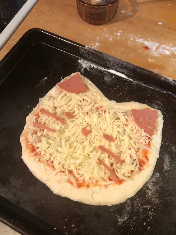 an uncooked pizza sitting on top of a black tray next to a wooden table