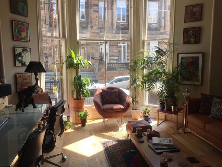 a living room filled with lots of furniture next to large windows and potted plants