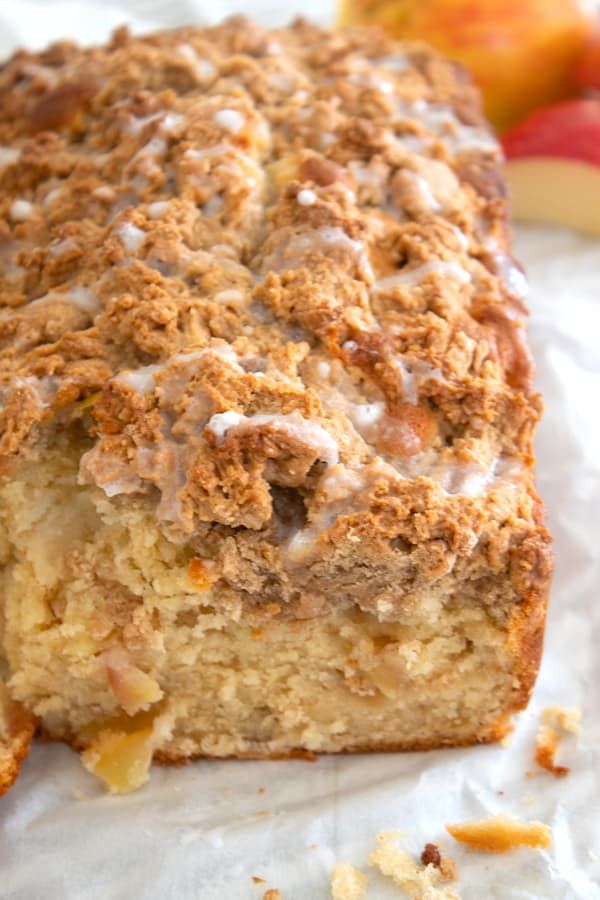 a close up of a piece of cake with icing and apples in the background