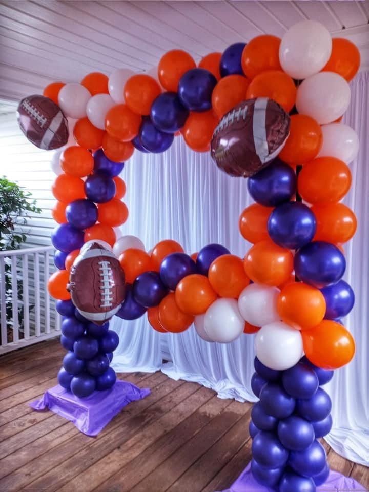 an arch made out of balloons with footballs on it and purple, orange and white colors