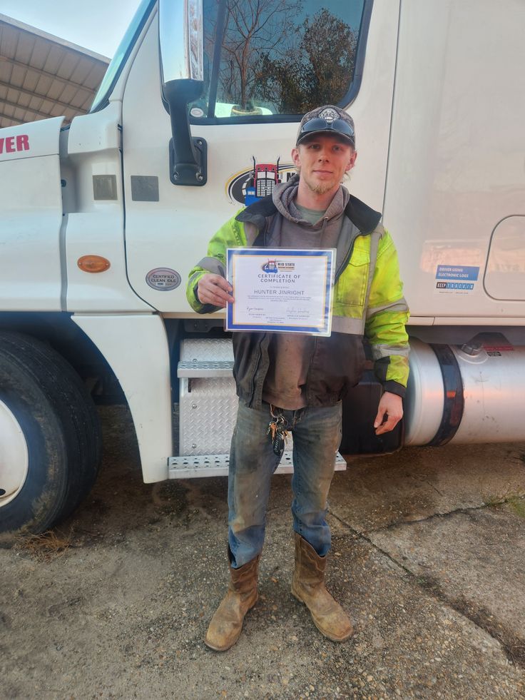 a man standing in front of a semi truck holding up a certificate for his work