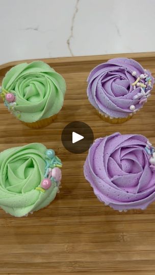 four cupcakes with different colored frosting on a wooden board