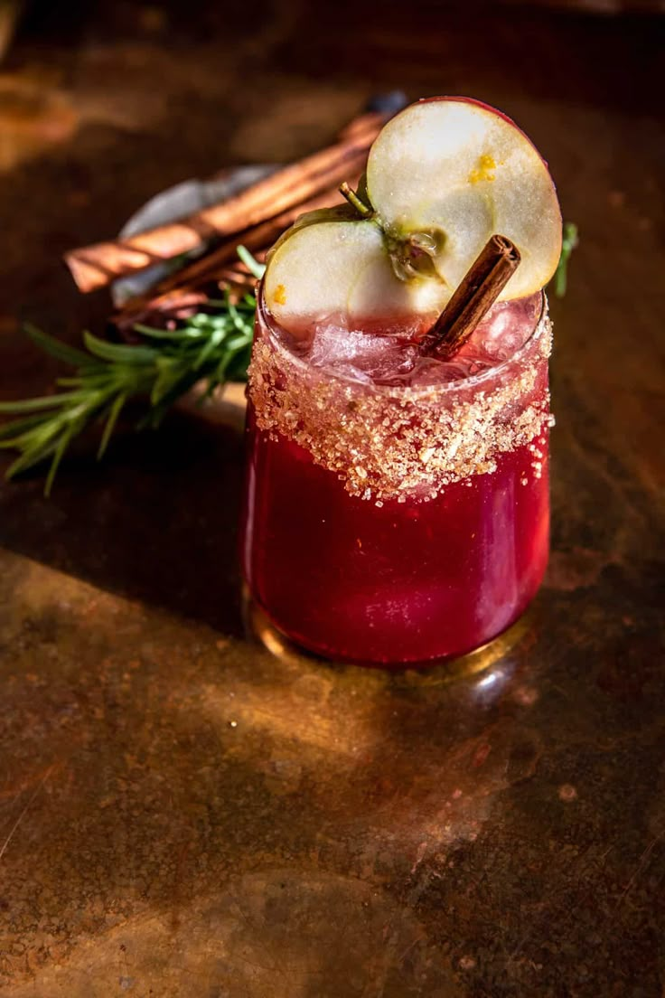 an apple sitting on top of a red drink in a glass with cinnamon sticks sticking out of it