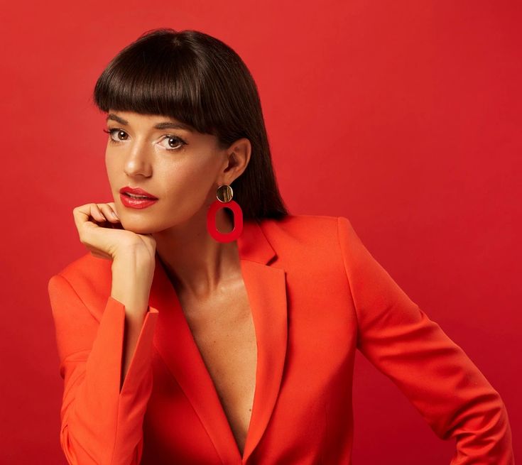 a woman in an orange suit posing with her hand on her chin