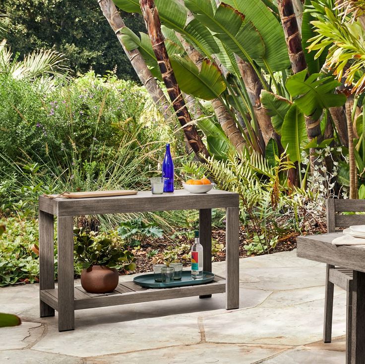 a wooden table sitting on top of a stone floor next to a lush green forest