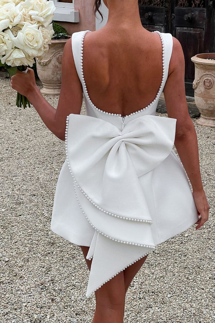 the back of a woman in a white dress holding flowers