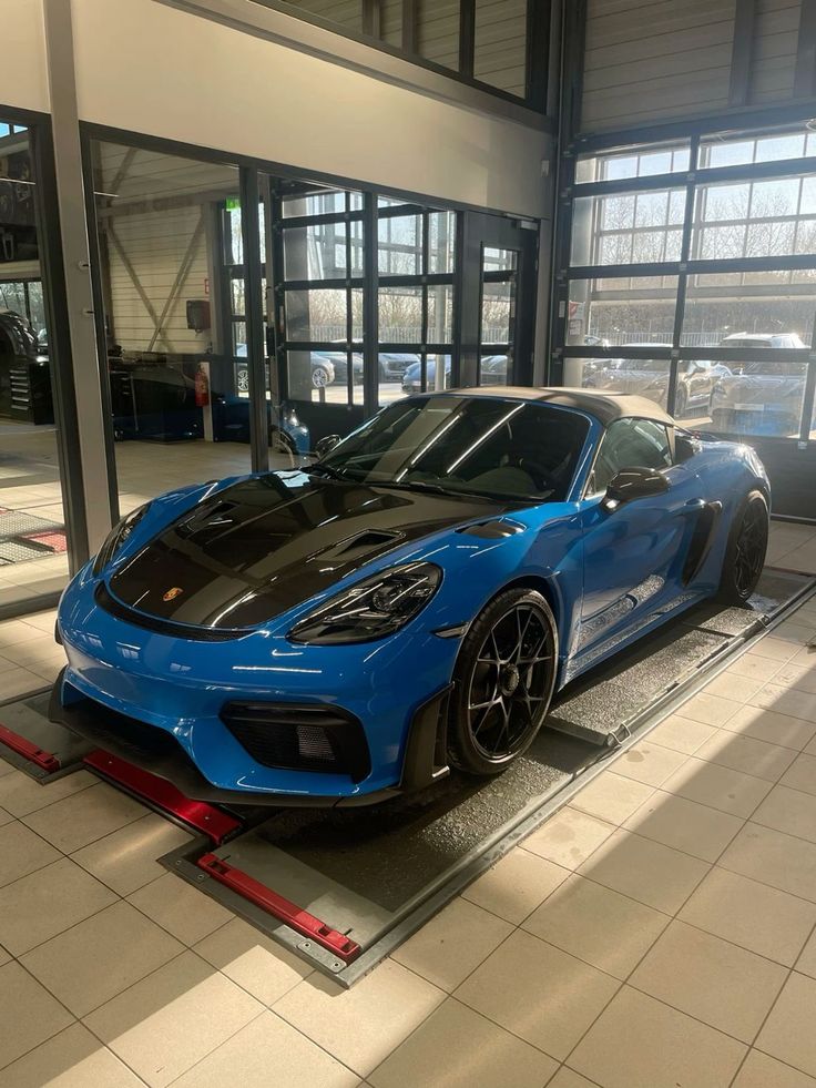 a blue sports car is parked in front of some glass windows and another one is on the ground