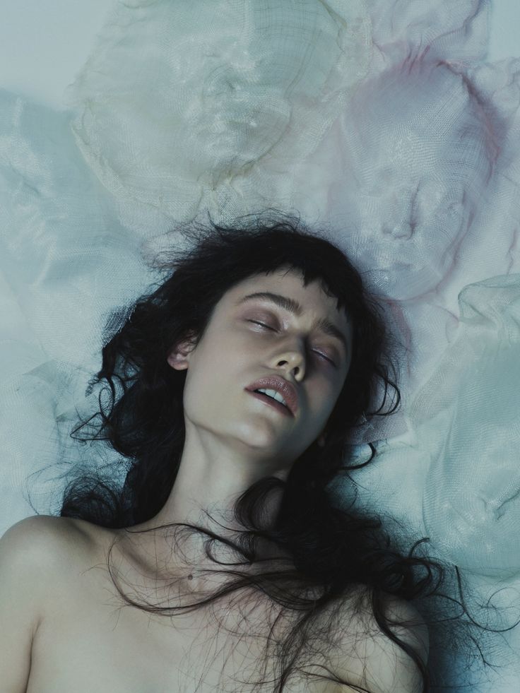 a woman laying on top of a bed covered in white sheets with her eyes closed