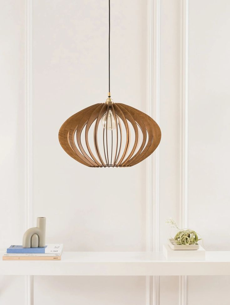 a wooden light fixture hanging over a white shelf next to a book on a table