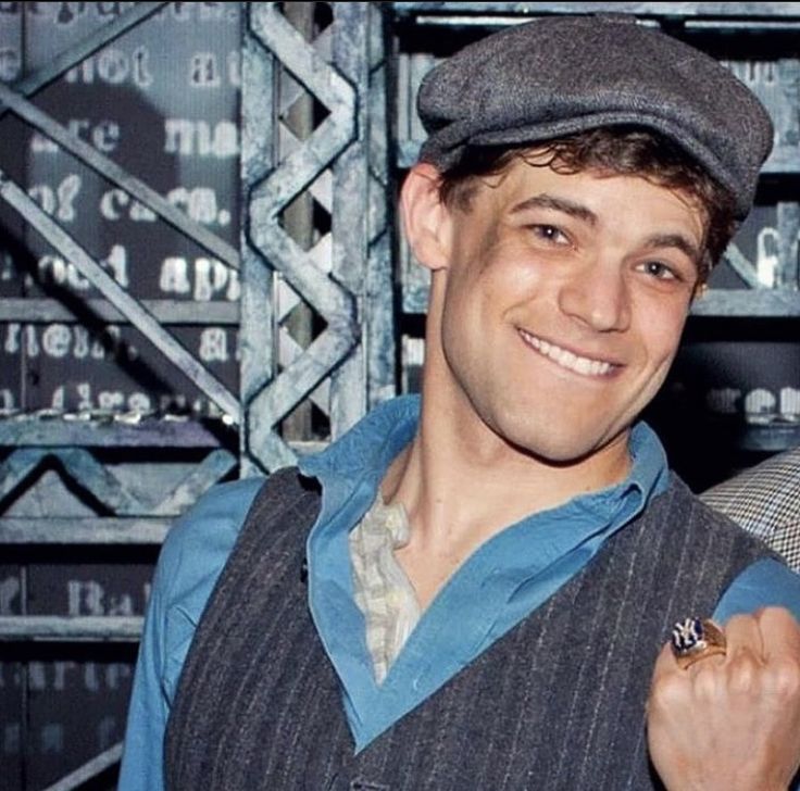 a man wearing a hat and vest with a ring on his left hand, smiling at the camera