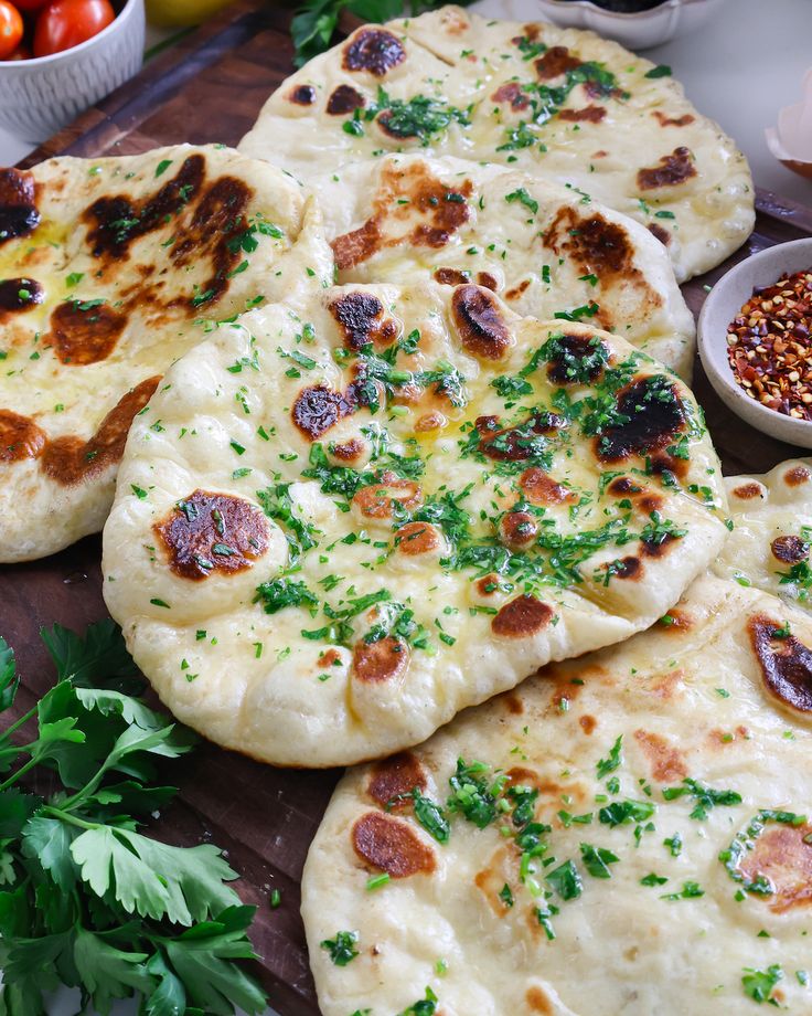 several flat bread pizzas on a cutting board with parsley and tomatoes in the background