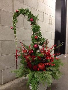 a vase filled with red berries and greenery on top of a floor next to a brick wall