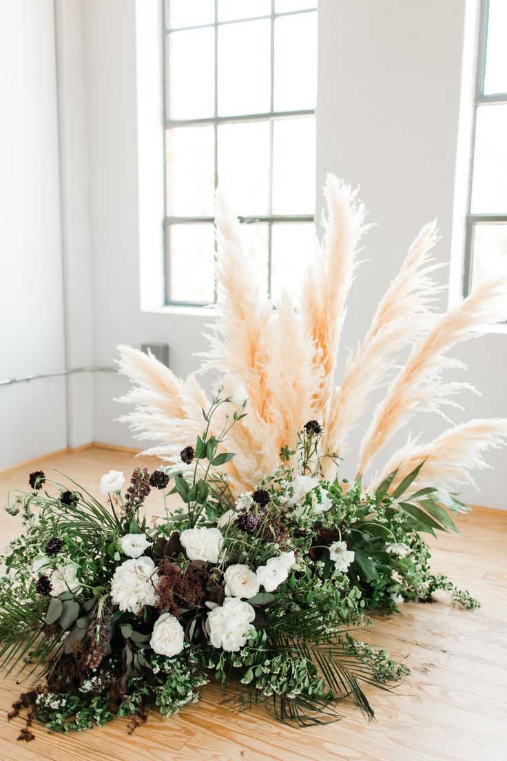 an arrangement of white flowers and greenery on a wooden table