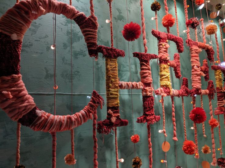 the wall is decorated with colorful yarn and pom - poms hanging from it's sides