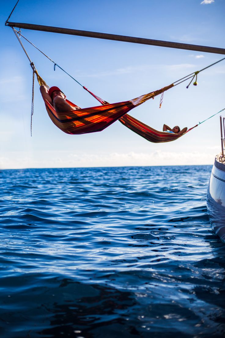 a man laying in a hammock on top of a sailboat near the ocean