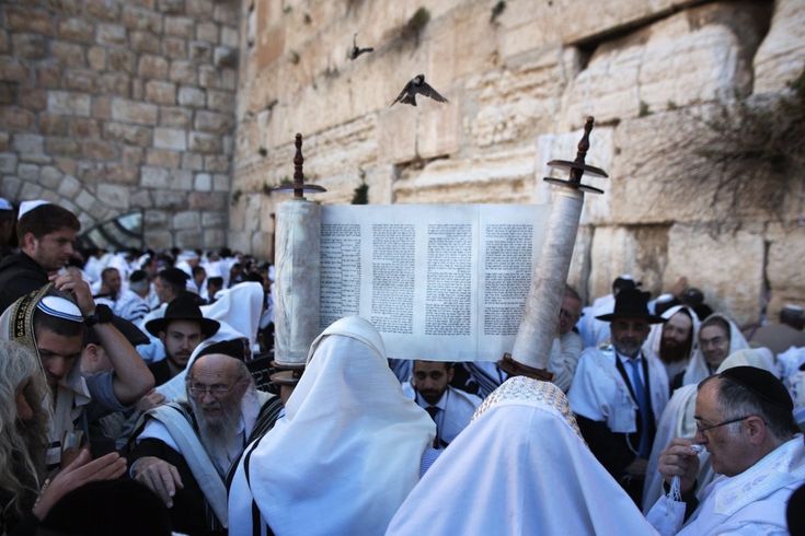 a group of people standing around each other in front of an old building with a large book on it's head