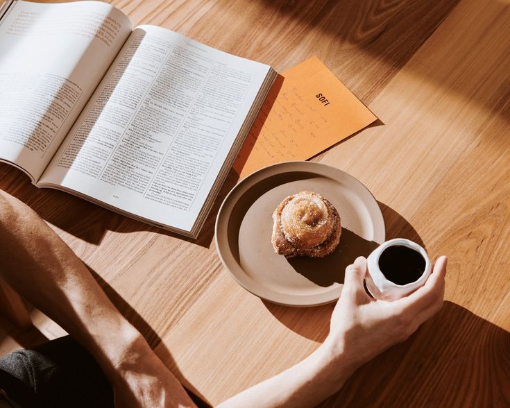 a person sitting at a table with an open book and cup of coffee in front of them