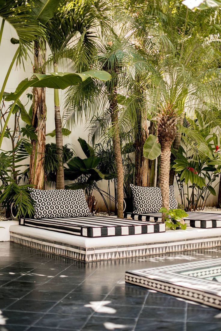 an outdoor seating area with black and white cushions, palm trees, and tiled flooring