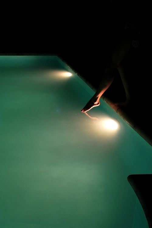 a person standing on the edge of a swimming pool with their feet in the water