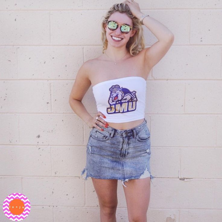 a young woman wearing sunglasses and a white top with the umc logo on it is standing in front of a brick wall