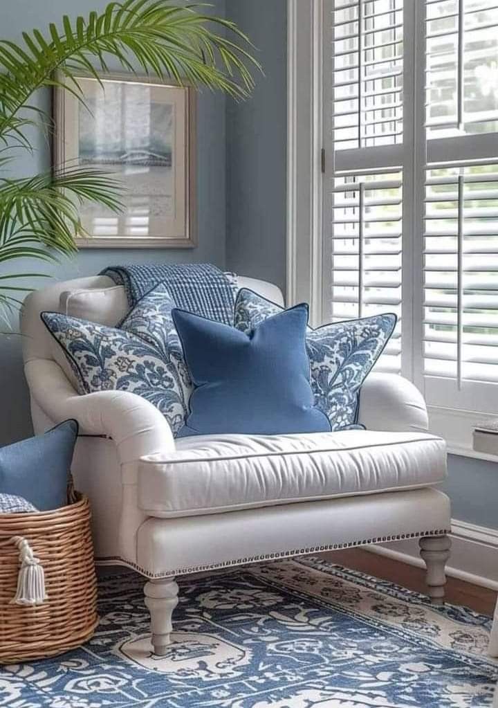 a living room with blue walls and white furniture, including a chair in front of a window