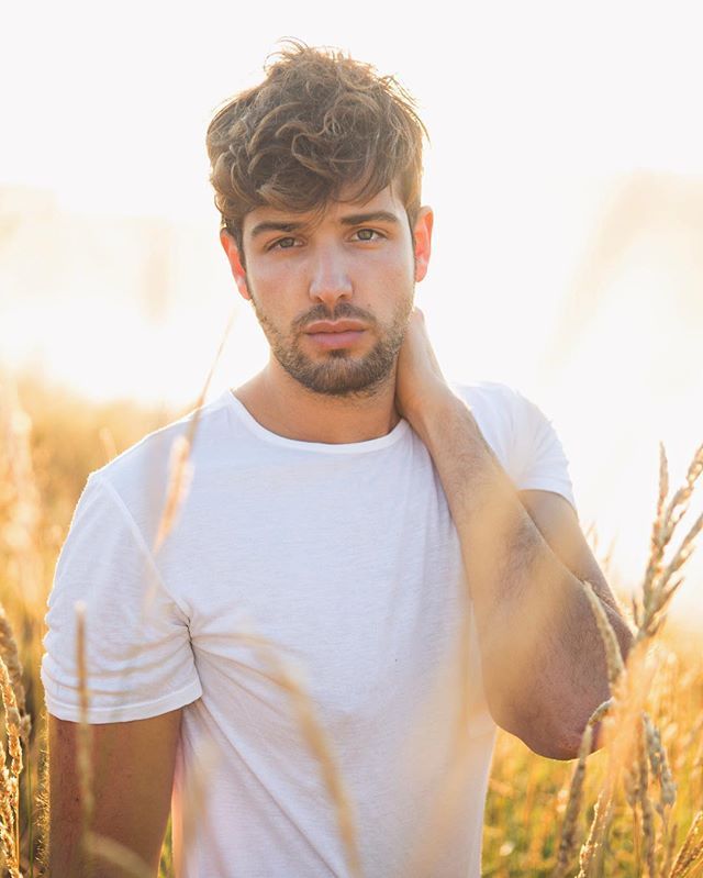 a man standing in the middle of a field with his hand on his ear and looking at the camera