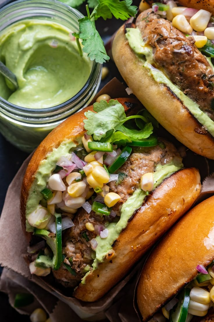 three sandwiches with avocado, corn and cilantro on them next to a jar of guacamole