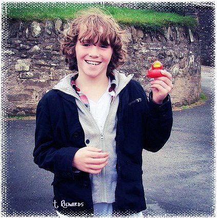 a young boy holding an apple in his right hand while standing next to a stone wall