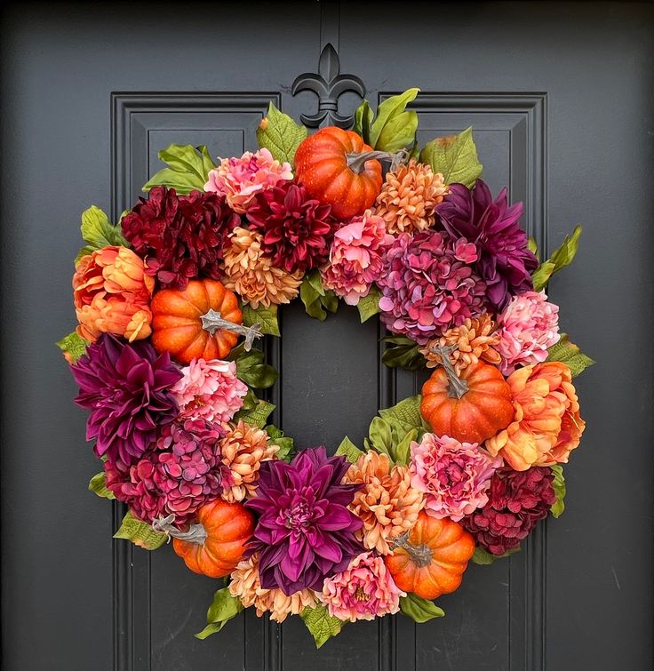 a wreath with flowers and pumpkins is hanging on the front door's black door