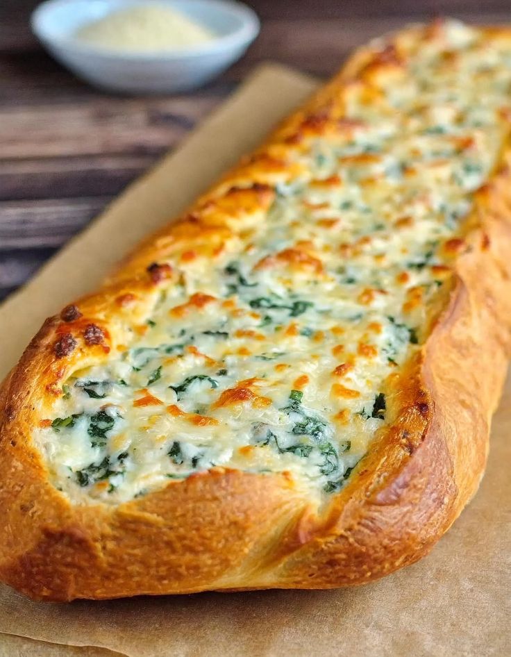 a cheesy bread with cheese and spinach on it sitting on a piece of wax paper