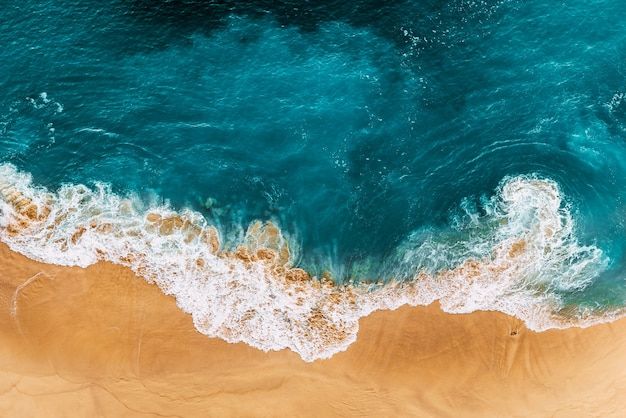 an aerial view of the ocean with waves crashing on it's shore and brown sand