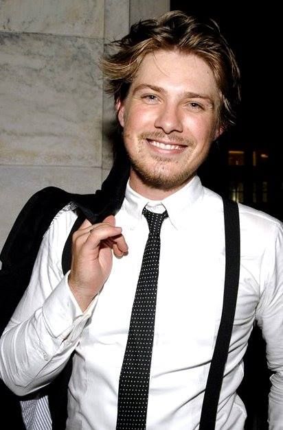 a young man wearing a white shirt and black tie smiling at the camera while holding his jacket over his shoulder