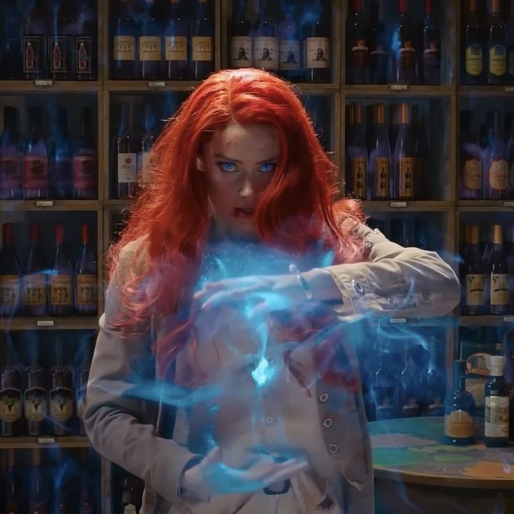 a woman with red hair and blue eyes holds up her hands in front of a shelf full of bottles