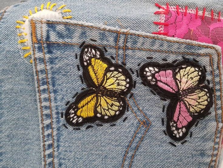 two butterflies are on the back of a pair of blue jean pants with pink and yellow accents