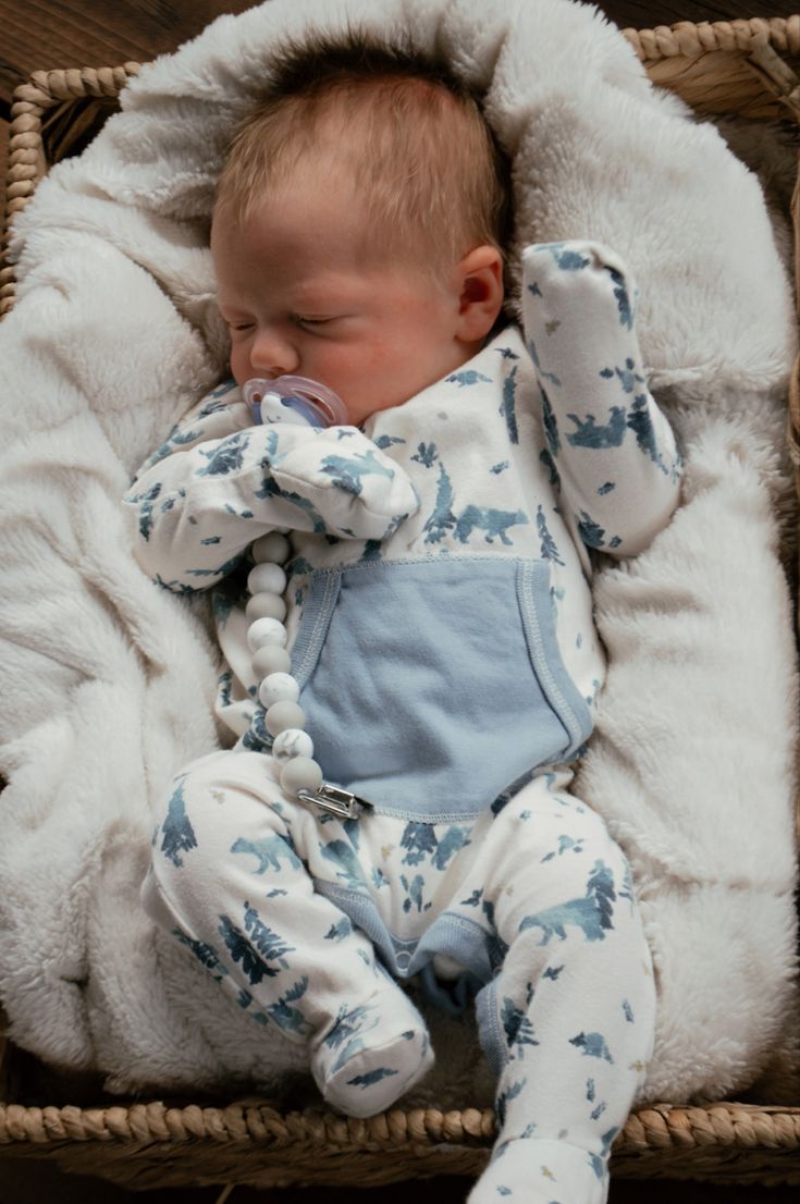 a baby is sleeping in a basket with a blanket on it's back and pacifier in its mouth