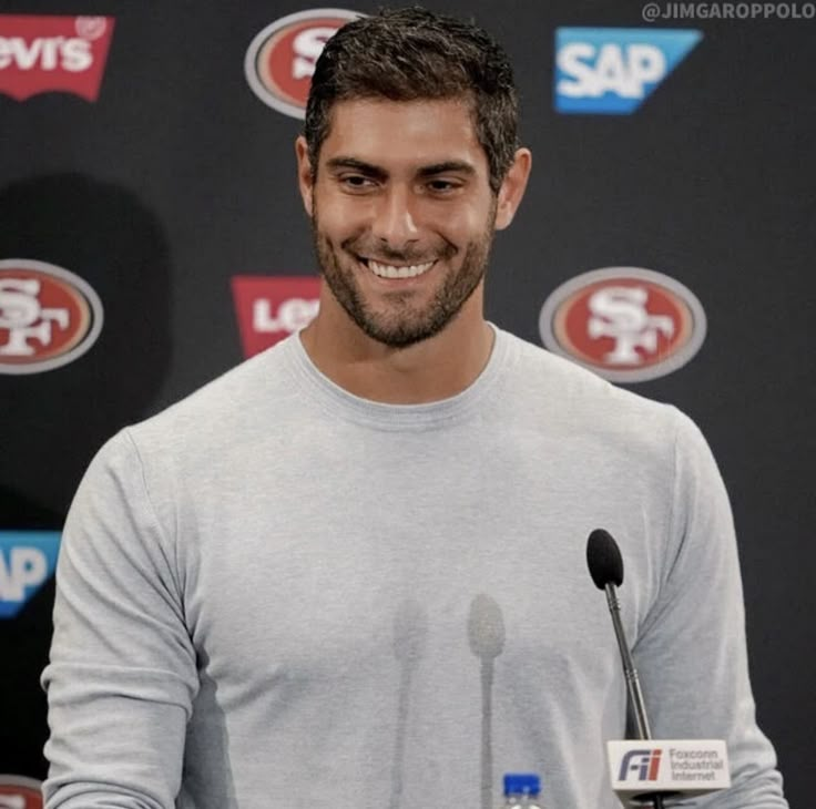 a man standing in front of a microphone at a press conference wearing a gray shirt