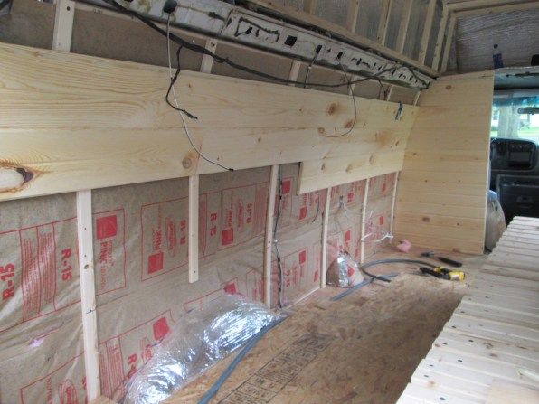 the inside of a truck with some wood on it's floor and insulation taped up