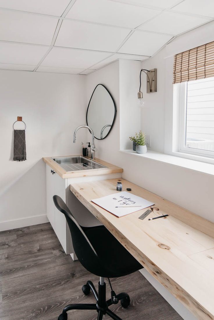 a desk and chair in a small room with a window, sink and mirror on the wall