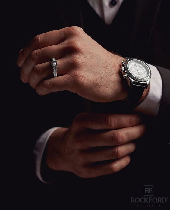 a man in a suit and white shirt holding onto his wrist with a watch on it