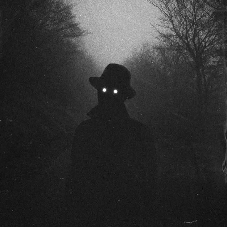 a person wearing a hat and light up eyes in the dark with trees behind them