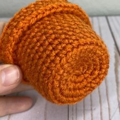 an orange crocheted object being held by someone's hand