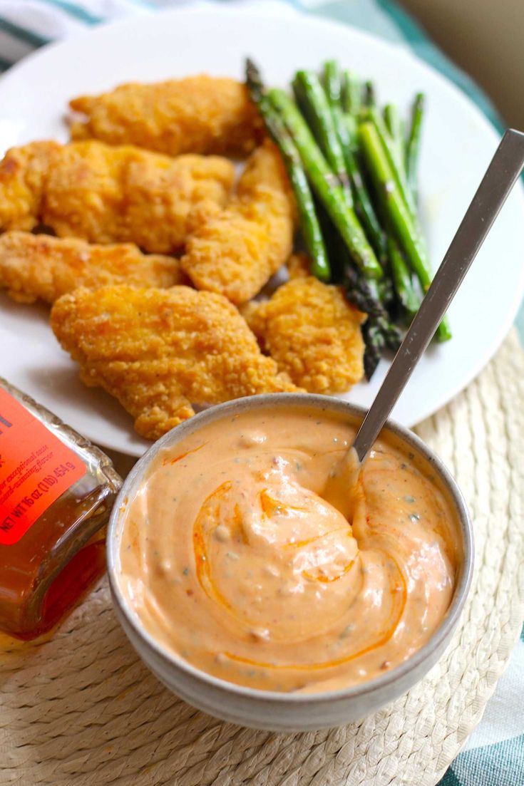 a white plate topped with fried chicken next to sauce and asparagus on a table