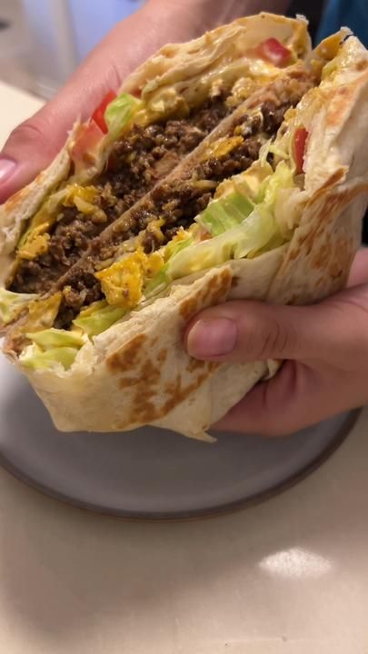 a person holding a burrito with meat and lettuce in it on a plate