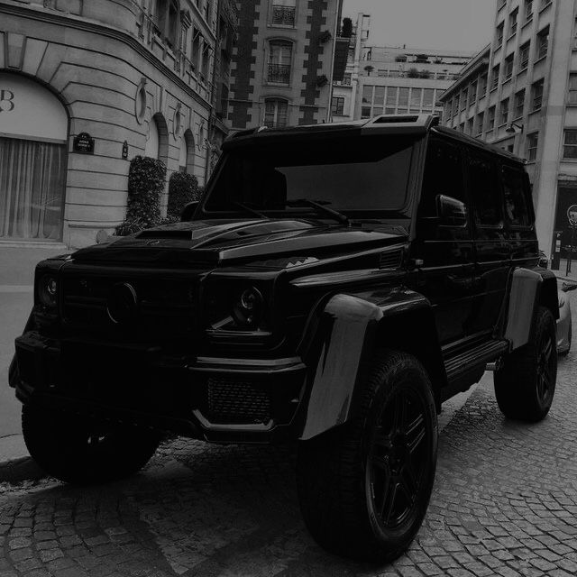 a black and white photo of a mercedes g - class parked in front of a building