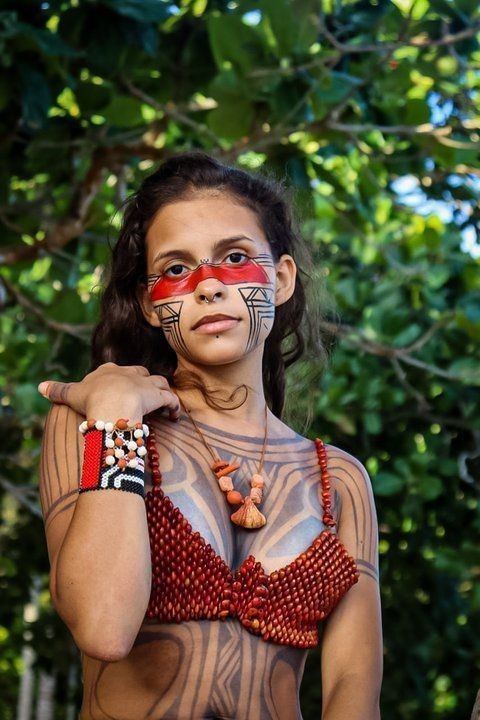 a woman with painted face and body art poses for the camera in front of some trees